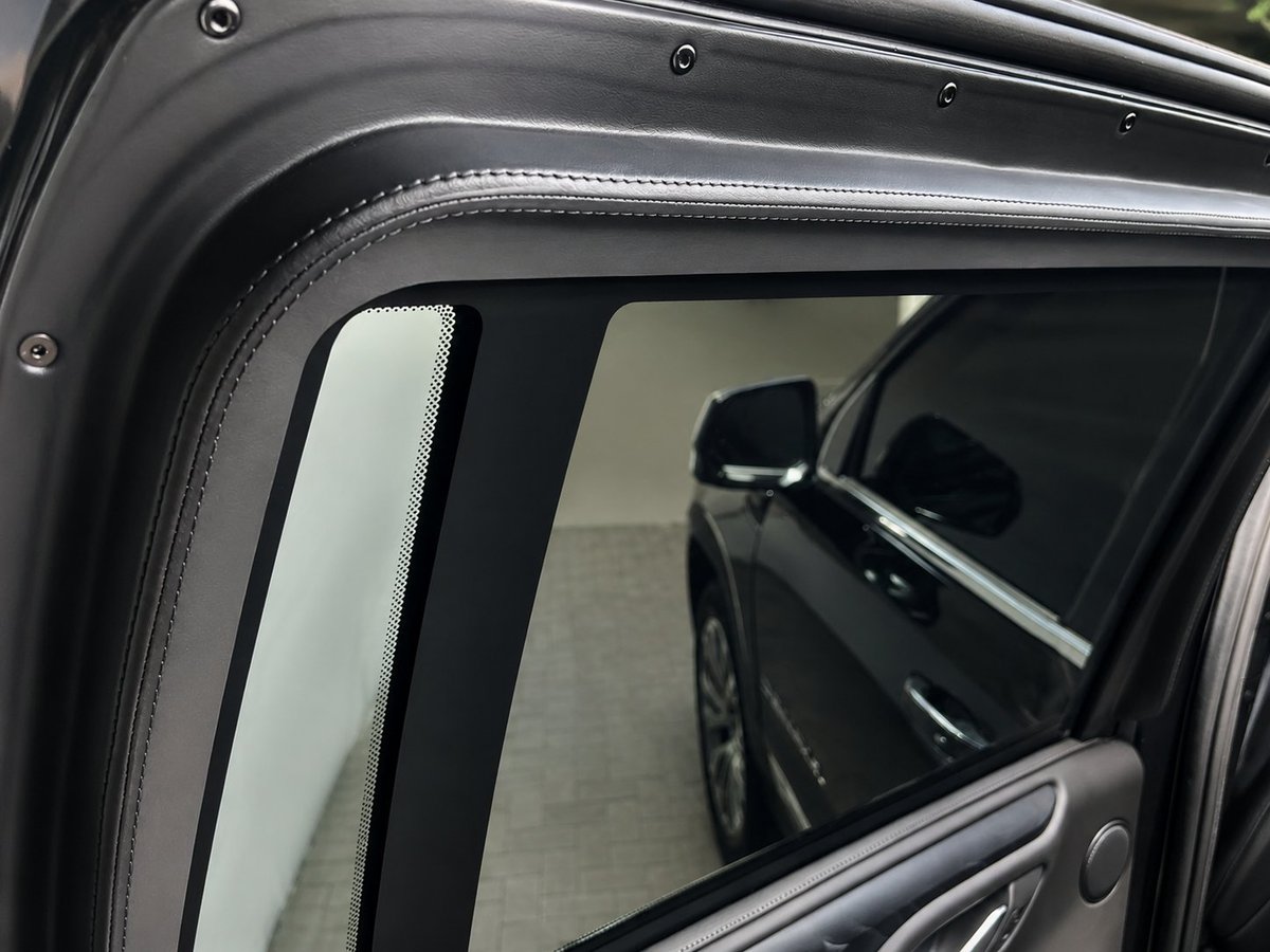 Close-up of a vehicles side window frame and mirror, showing the trim detail and interior reflection of another car.